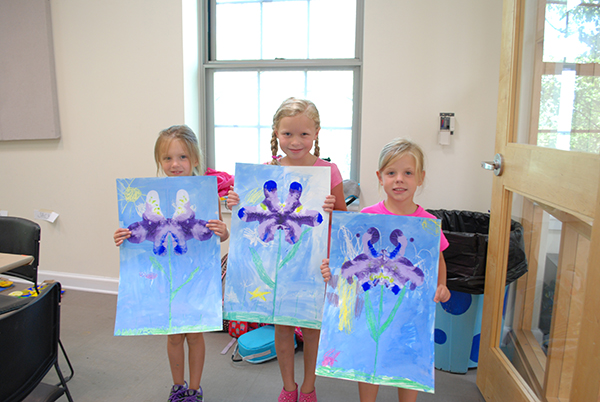 Three girls holding paintings for Bugs and Blooms